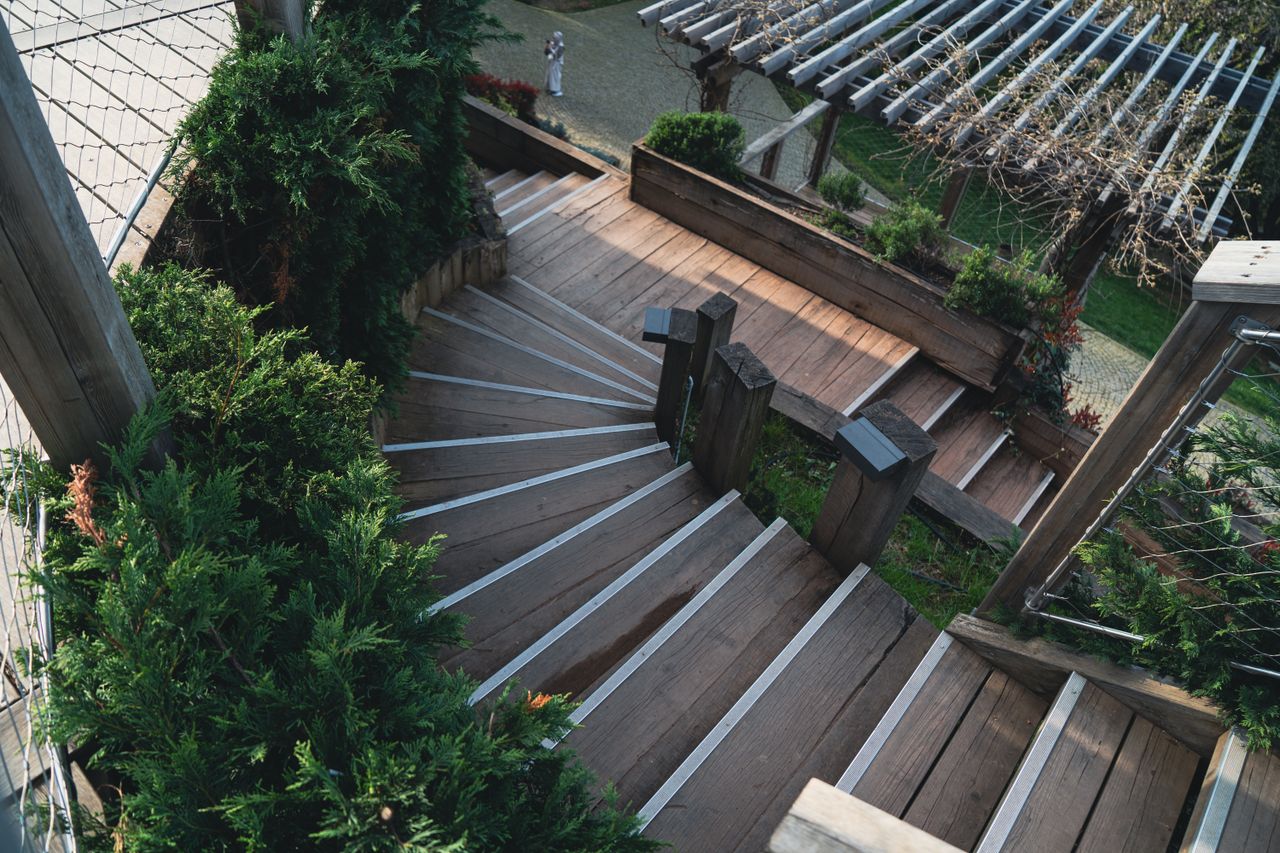 Home Explore the elegance of a wooden staircase surrounded by lush greenery in an outdoor garden.